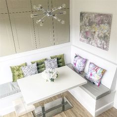 a white table with some colorful pillows on it and a bench in front of it