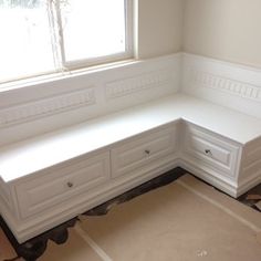 a corner bench in the middle of a room with white walls and trim around it