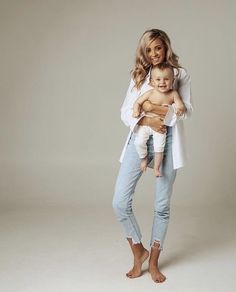 a woman holding a baby in her arms and smiling at the camera while standing against a white background