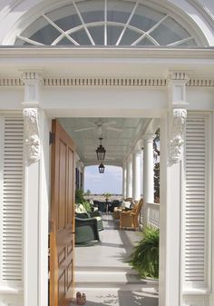 an open door leading to a porch with chairs and potted plants on either side