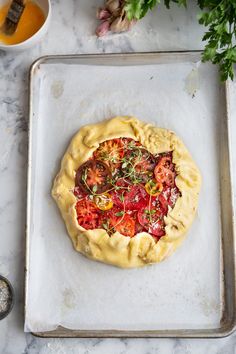 an uncooked pizza sitting on top of a metal tray next to some vegetables