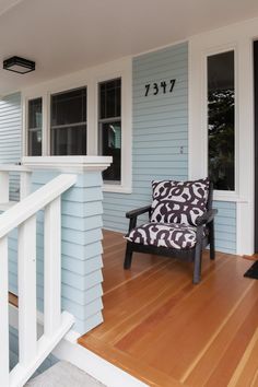 a chair sitting on the front porch of a blue house with white trim and wood flooring