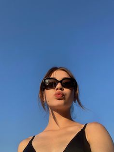a woman wearing sunglasses blowing bubbles in the air while standing under a clear blue sky