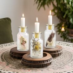 three glass bottles with flowers and feathers in them sitting on a wooden stand next to a potted plant