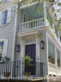 a white house with a purple door and black iron railing on the front porch is surrounded by trees