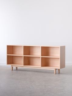 a wooden shelf with four compartments on one side and two legs, in front of a white wall