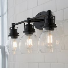 three clear globe lights are hanging from the bathroom light fixture in front of a white tiled wall