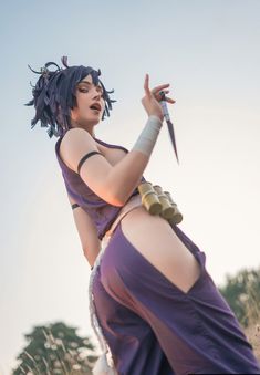 a woman in a purple dress holding a knife up to her chest and looking off into the distance