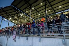 a group of people standing next to each other near a fence and some fans on the bleachers