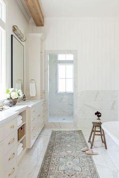 a bathroom with white walls and marble flooring, along with a rug on the floor