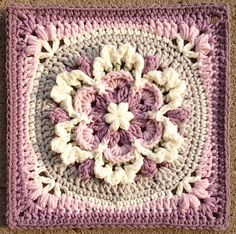 a crocheted square with pink and white flowers in the center, on carpet