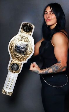 a woman holding up a white and gold wrestling belt with tattoos on her arm while standing in front of a gray background