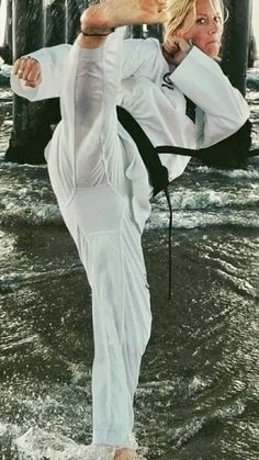 a woman in white is doing karate on the water with her leg up and one hand behind her head