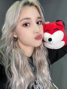 a woman with long grey hair holding a stuffed animal in front of her face and looking at the camera