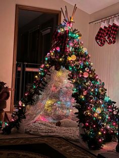 a decorated christmas tree in the corner of a room with stockings hanging from the ceiling