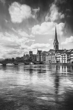 a black and white photo of a river with buildings on the bank in the background