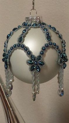 a white ornament with blue beads hanging from a metal hook on a wall