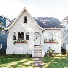 a small white house with windows and plants in the window boxes on the front door