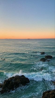 people are swimming in the ocean at sunset