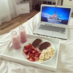 a laptop computer sitting on top of a bed next to a plate of fruit and cookies