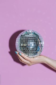 a woman's hand holding a disco ball against a pink background