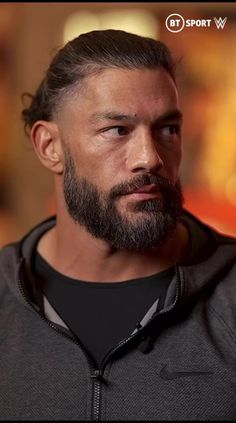 a close up of a man with a beard wearing a hoodie and looking at the camera