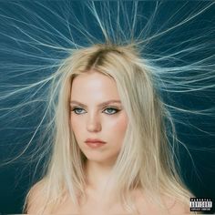 a woman with long blonde hair and blue eyes looking at the camera, while she has her hair blowing in the wind