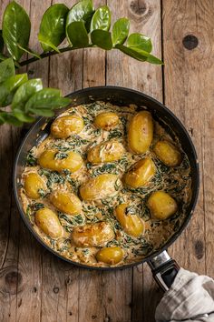 a pan filled with potatoes and spinach on top of a wooden table