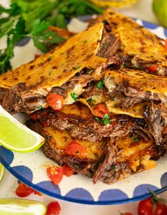 a blue and white plate topped with quesadillas next to lime wedges