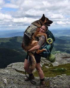 a woman holding a dog on top of a mountain