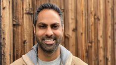 a man with a goatee smiles at the camera while standing in front of a wooden fence