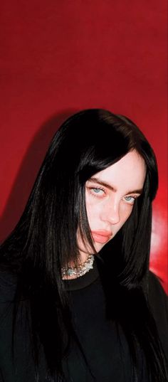 a woman with long black hair standing in front of a red wall