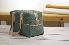 a green quilted bag sitting on top of a wooden table next to a white towel