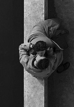 black and white photograph of two people leaning against a wall, one holding the other's head