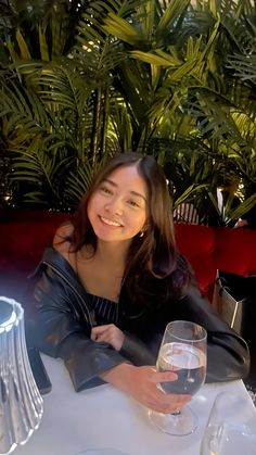 a woman sitting at a table with a glass of wine in front of her smiling