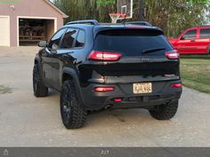 the back end of a black jeep parked in front of a garage with basketball hoop