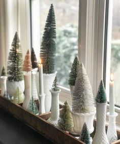 small christmas trees in white vases on a window sill next to candles and windowsill