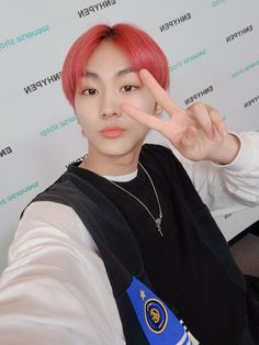 a young man with pink hair making the peace sign while sitting in front of a white wall