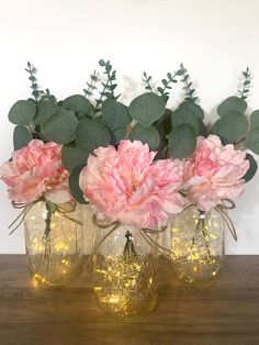 three vases filled with pink flowers on top of a wooden table next to greenery