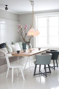 a dining room table and chairs with flowers in vases on the end, next to a couch