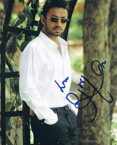 an autographed photo of a man leaning against a gate with trees in the background