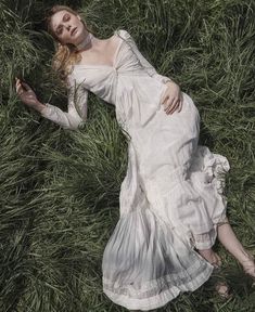 a woman laying in the grass wearing a white dress