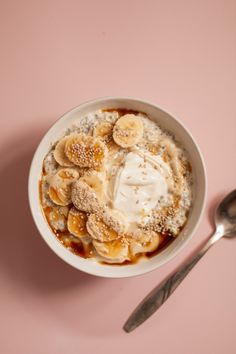 a bowl of oatmeal topped with bananas and whipped cream next to a spoon