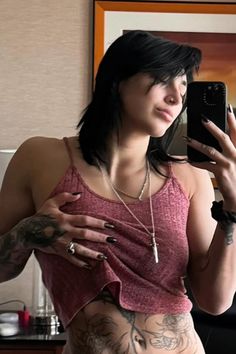 a woman with tattoos taking a selfie in the mirror while holding a cell phone