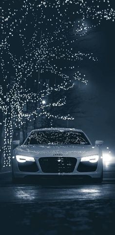 a car parked in front of a tree with lights on it's headlight