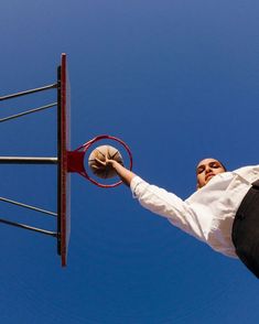 a man holding a basketball up to the rim of a basketball hoop in front of a blue sky