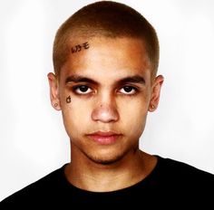 a young man with tattoos on his forehead and nose is looking at the camera while wearing a black t - shirt