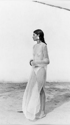 a woman is standing on the beach wearing a long dress