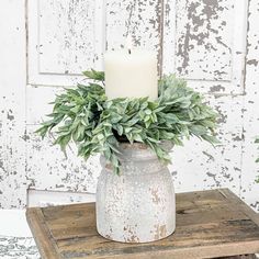 a white candle sitting on top of a wooden table next to a green plant in a vase