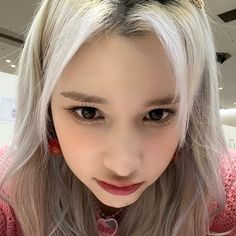 a girl with grey hair and pink sweater looking at the camera while holding a cell phone